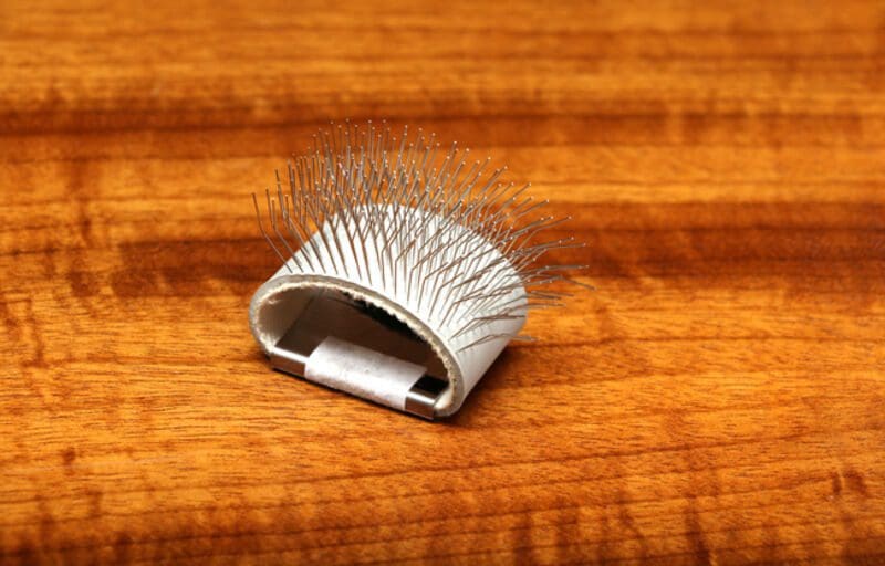 A white hairbrush with metal bristles on a wooden surface.