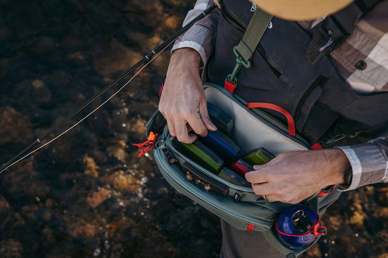 Person organizing fishing gear in a waist pack near water.
